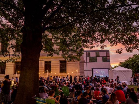 Wide view of visitors sitting on Huntington Avenue lawn, ready for Sunset Cinema screening