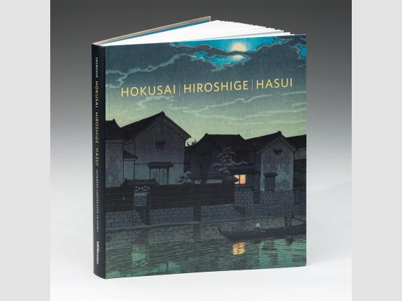 Image of book cover Hokusai, Hiroshige, Hasui. The cover features a print of houses along a river at dusk. A boat is on the river and the moon is visible through the clouds. A window in one house is lit and reflects on the water.