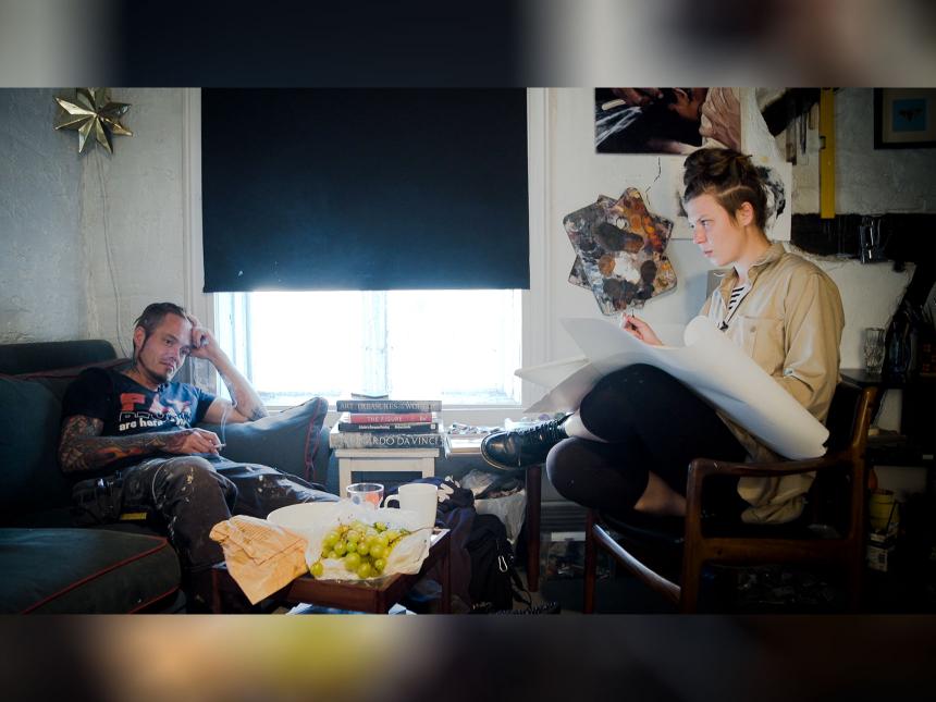 film still from The Painter and the Thief, depicting man and woman sitting in room across from one another