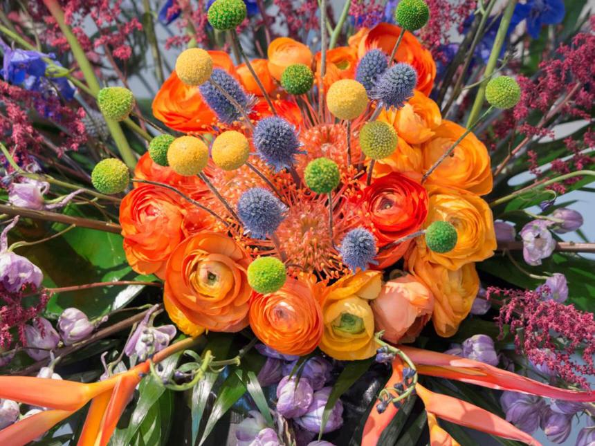 Detail of brightly colored floral arrangement with large orange bloom in the center surrounded by smaller purple and yellow poms