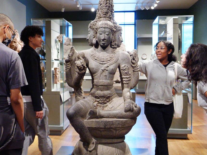 Teens standing around and looking at stone sculpture depicting multi-faced Hindu god