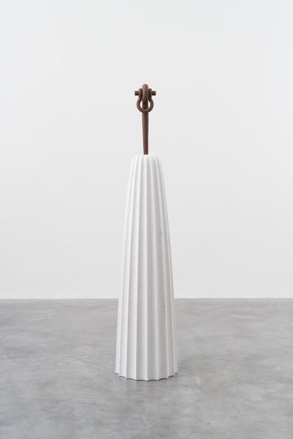 A tapered white column with a cast-iron rod sticking out of the top; the rod is ornamented at top with a shackle.
