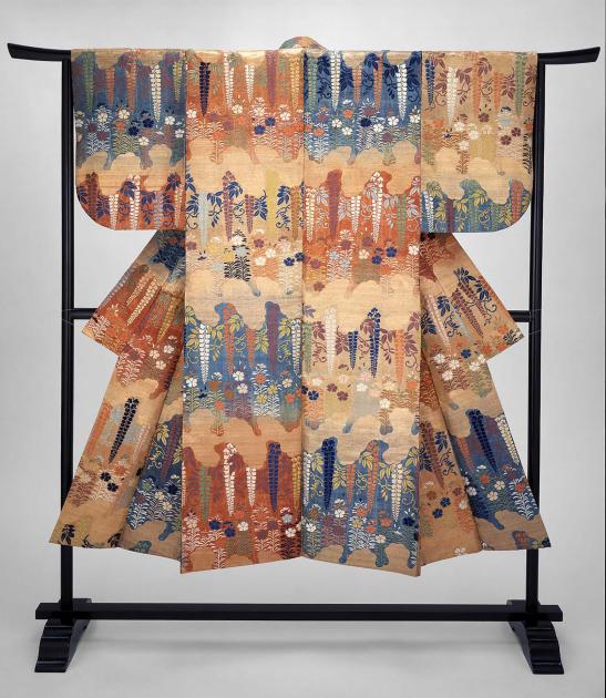 A richly ornamented blue, orange, and yellow robe hanging on a black rack so it is splayed to show the entire surface.