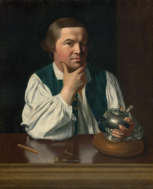 Man sitting at a table resting his chin in his hand looking at the viewer