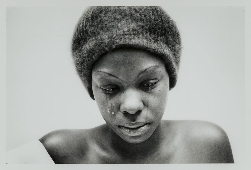 A woman shown from the shoulders up looks down as tears fall from her eyes.