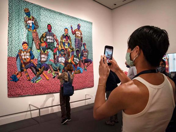 College student in foreground taking photo of Bisa Butler quilt, To God and Truth, in Fabric of a Nation exhibition