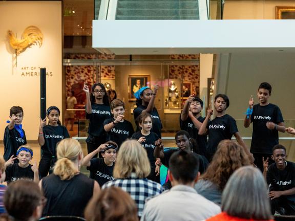 A group of children signs in ASL to a crowd.