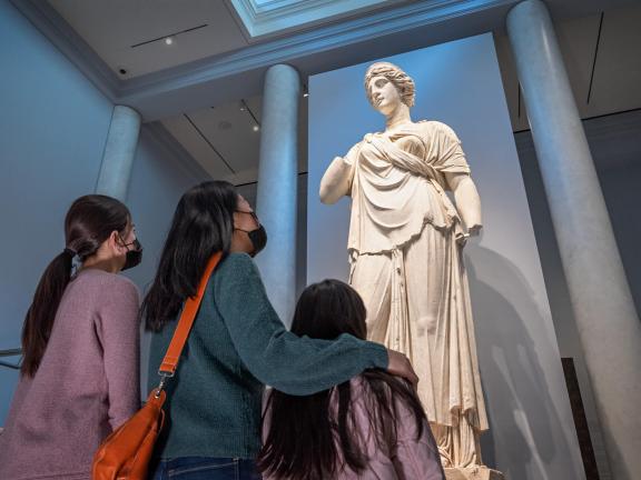 Three visitors (one adult and two children) look up at large Greek sculpture of Juno in Gods and Goddesses gallery