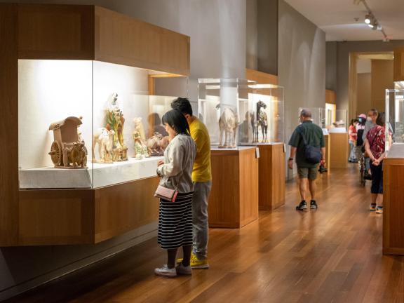 Two visitors looking at Chinese ceramic sculptures of camels and ox-drawn carts inside display case