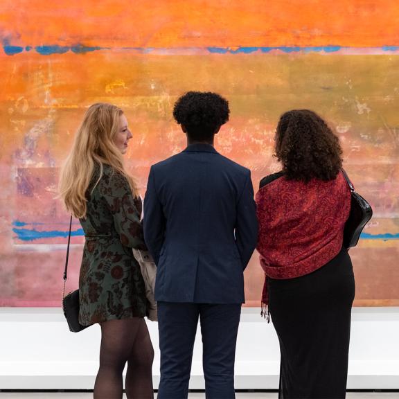 Three visitors view a painting in the Frank Bowling's Americas exhibition.