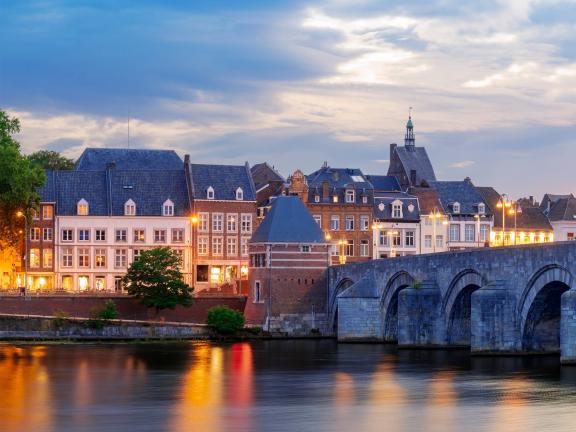 An illuminated row of houses on one side of a stone bridge in Maastricht, Netherlands.