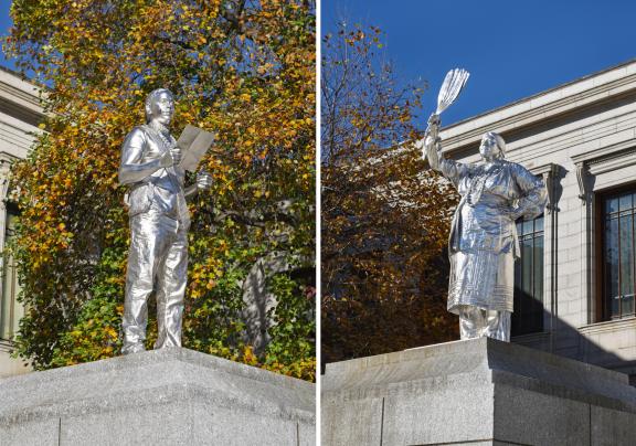 At left, a silver sculpture of Andre StrongBearHeart Gaines Jr. reading from piece of paper; at right, a silver sculpture of Julia Marden in traditional regalia holding up fan made of turkey feathers