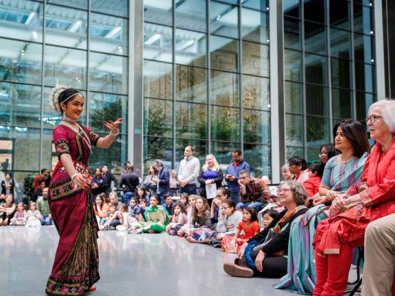 A woman stands in front of a crowd and dances in a dark red outfit.