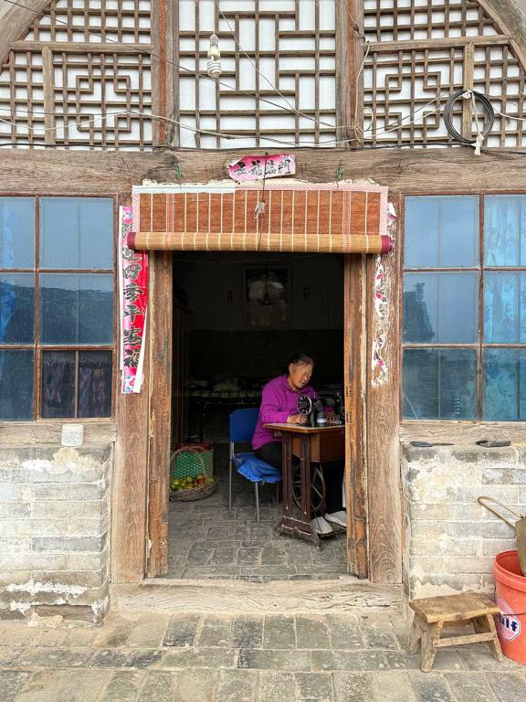 A woman sits in a darkened doorway and works at a sewing machine.
