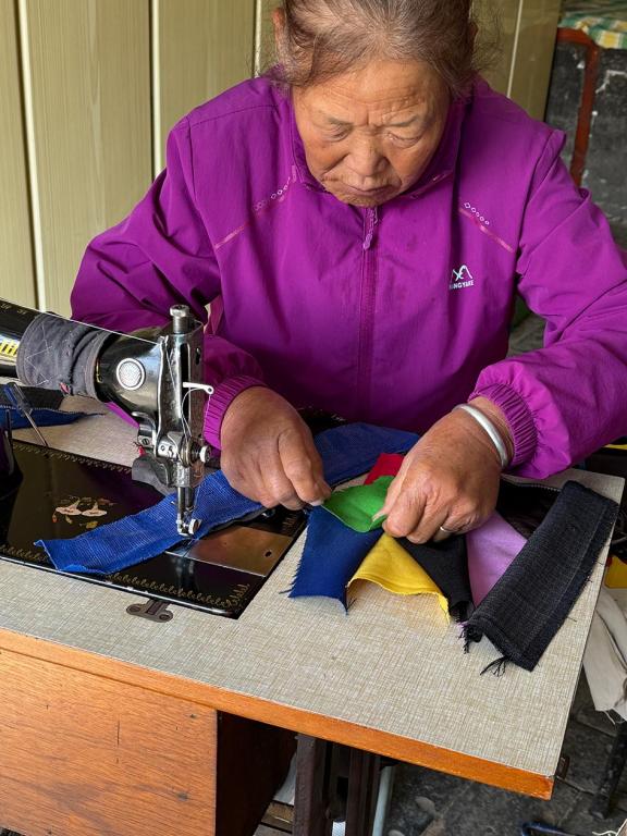A woman pieces together bits of fabric at a table with a sewing machine.