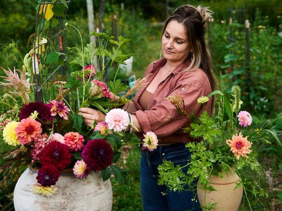 A woman outside in a garden works on arranging flowers
