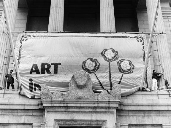 Black-and-white archival photograph of an Art in Bloom banner being installed on the MFA building in the 1970s.