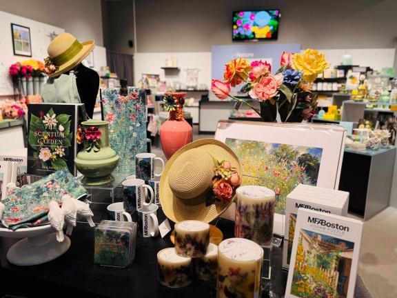 Display of mugs, books, hats, and candles, all garden themed on table in exhibition shop