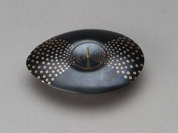 A disc-like, oblong smooth metal vessel with gold ornamentation