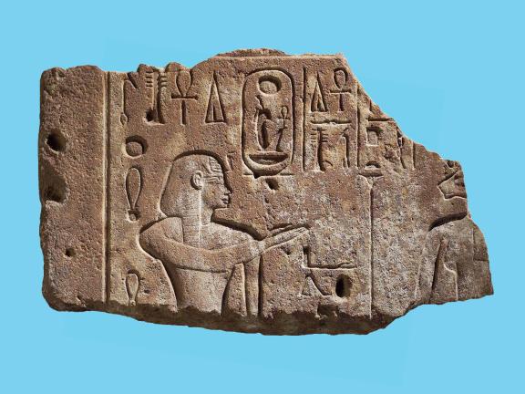 A quartzite carving in sunk relief showing Amenhotep III with a right hand raised toward before the lion-headed Sekhmet, who is barely seen due to the broken nature of the fragment. 