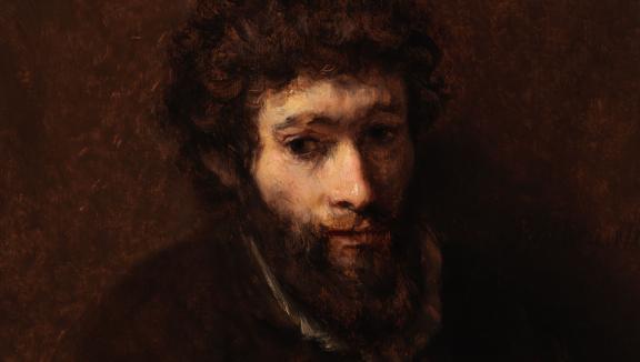 A young bearded man against a dark brown background.
