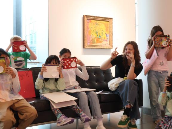 Teaching assistant with group of young students pretend to take photos with DIY cameras in gallery (SAC)