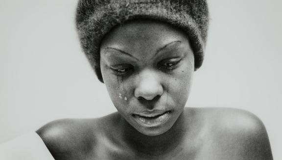 A woman shown from the shoulders up looks down as tears fall from her eyes.
