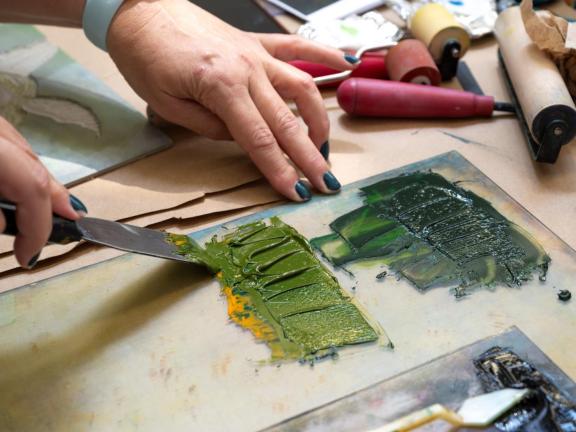hand scrapes green ink off palette with brayer (SAC)