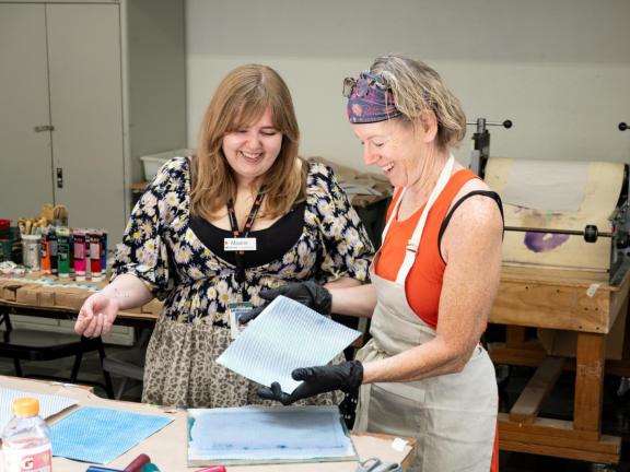 Printmaking instructor laughs with adult student looking at prints in classroom (SAC)