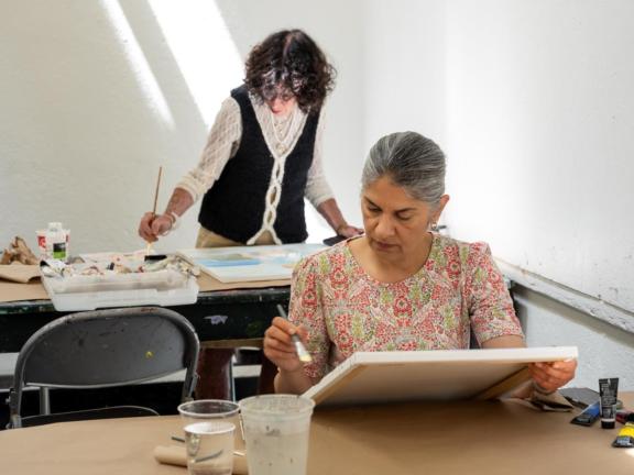 Two adult female students paint with watercolor at table in classroom (SAC)