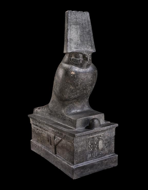 Stone statue of a falcon on top of a large base with inscriptions on its surface.