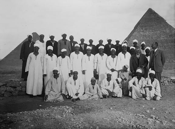 A group of men standing and smiling in front of the pyramids of Khufu and Khafra.