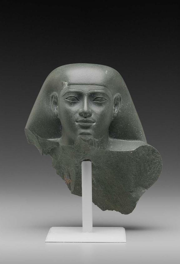 A stone fragment of an Egyptian man cut off around the shoulders.