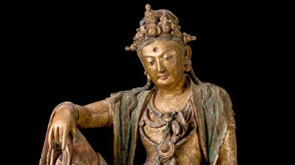 A wooden sculpture depicting Guanyin in seated position with hand on one raised knee