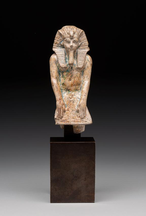 Tan stone statue of a shirtless Egyptian man with his arms relaxed in front of him.