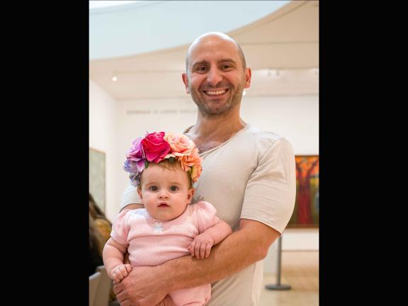 A smiling father holds a baby wearing a flower crown