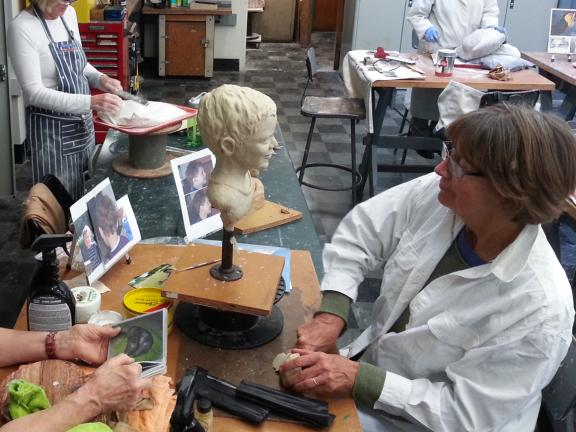 Woman sculpts clay bust of child in sculpture class