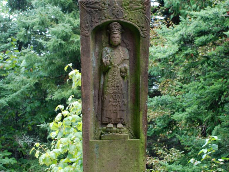 Bodhisattva figure carved into a niche on a large stone slab standing in a garden