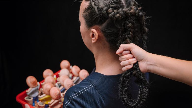 A hand tugs on a woman's braided hair.