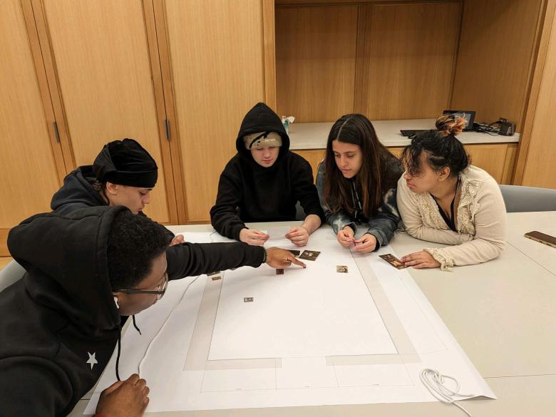Five teenagers sit closely around a large table and work collaboratively on a project 