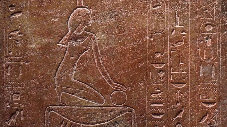 A stone engraved with a stylized woman kneeling, surrounded by hieroglyphics.