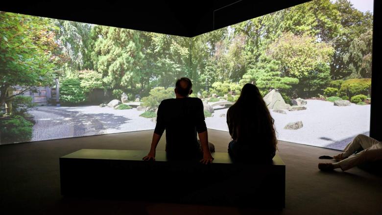 Two people look at a projection of a zen garden in a dark room.