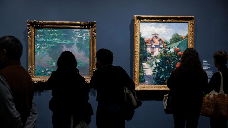 People look at Impressionist art framed and hung on a wall.