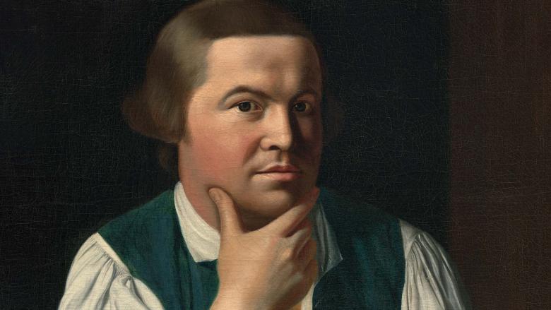 Man sitting at a table resting his chin in his hand looking at the viewer