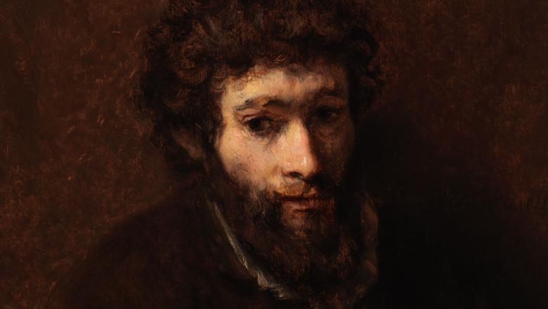 A young bearded man against a dark brown background.