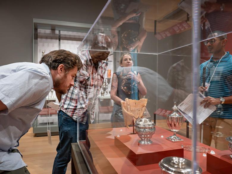 Educators looking inside glass case with ornate silver vessels on display
